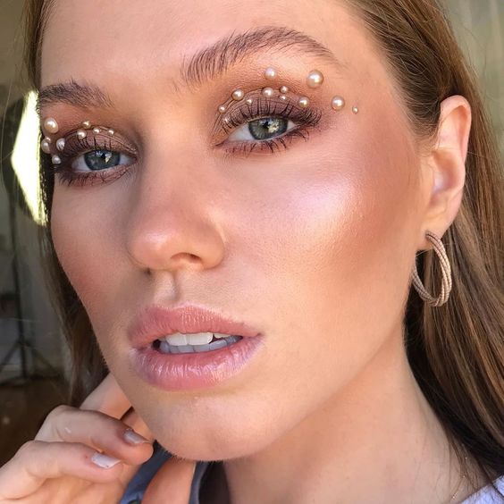 Mujer rubia con maquillaje luminoso y perlas