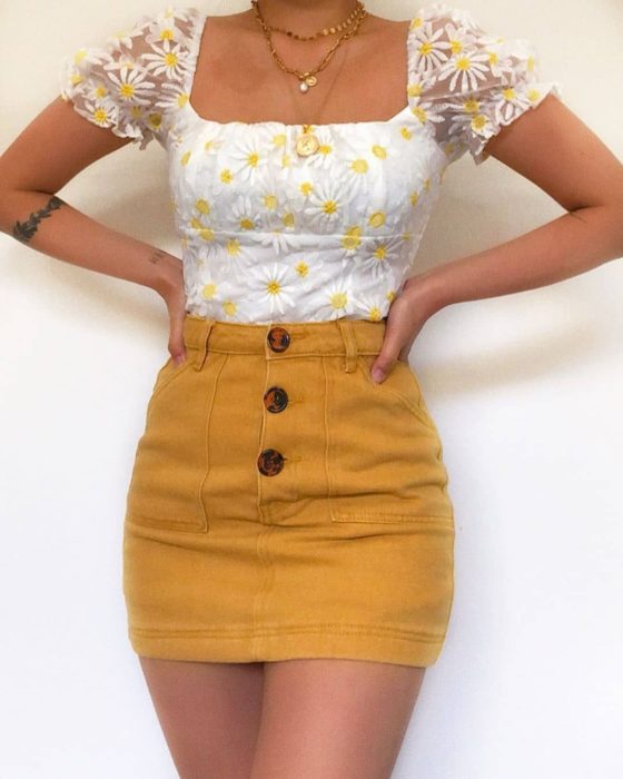 Chica usando mini falda color mostaza y blusa blanca con detalles de girasoles