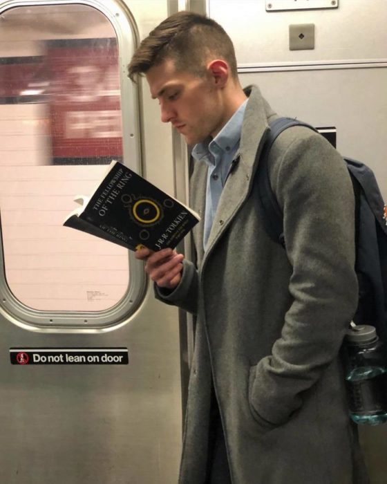 Hombre con gabardina gris y camiseta azul leyendo en el metro