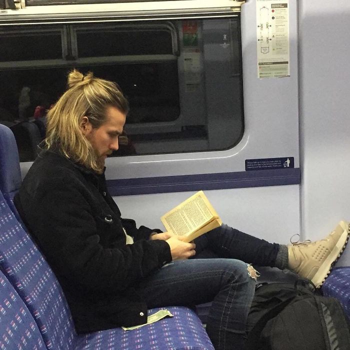 Hombre de cabello largo con peinado estilo bun leyendo dentro del metro