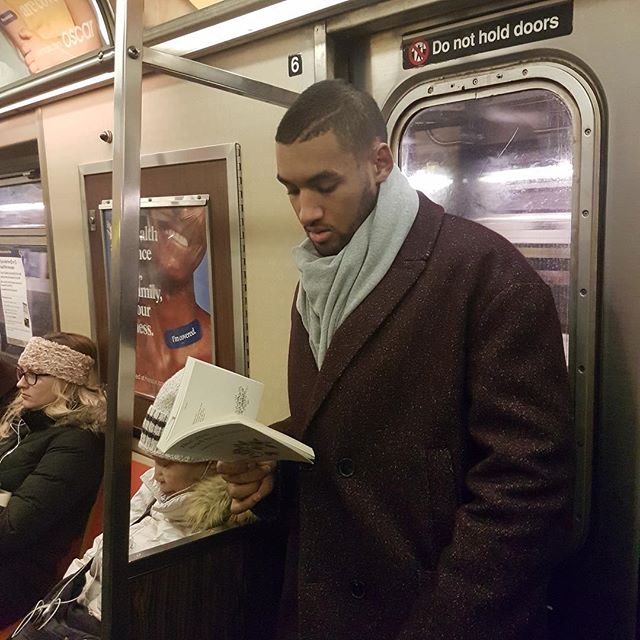 Hombre llevando bufanda azul cielo y abrigo café leyendo dentro del metro