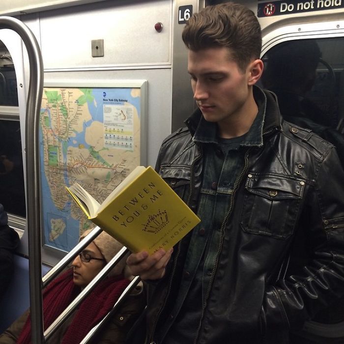 Chico leyendo un libro dentro del metro y llevando chamarra negra