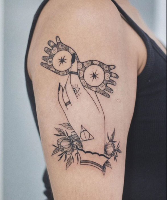 Tatuaje inspirado en Harry Potter, de una mano sosteniendo los lentes que usa Luna y otros detalles de la saga