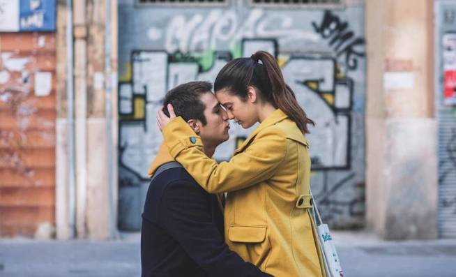 Escena de la película Amar, un chico abrazando a su novia con sao amarillo frente a una bodega
