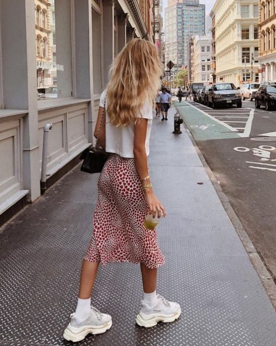 Chica rubia con blusa blanca, falda midi roja y tenis blancos