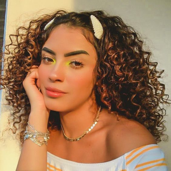 Chica rizada con cabello suelto y con dos broches en la parte delantera de la cabeza