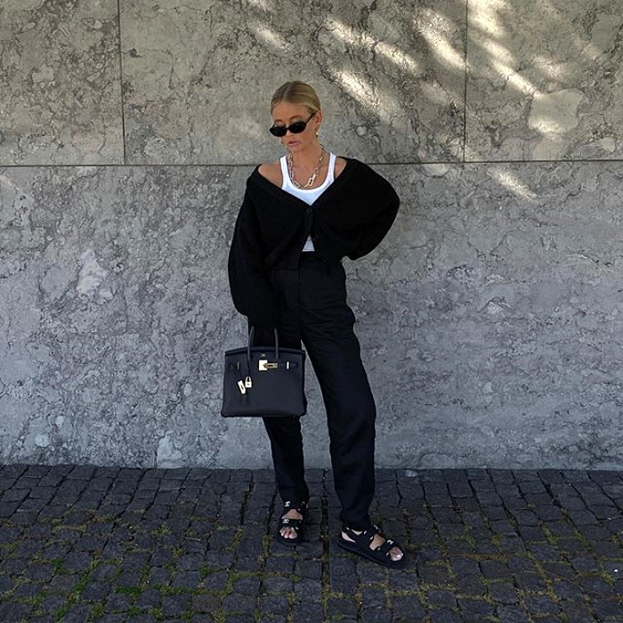 chica rubia con lentes de sol, top blanco de tirantes, suéter negro y pantalón de vestir negro