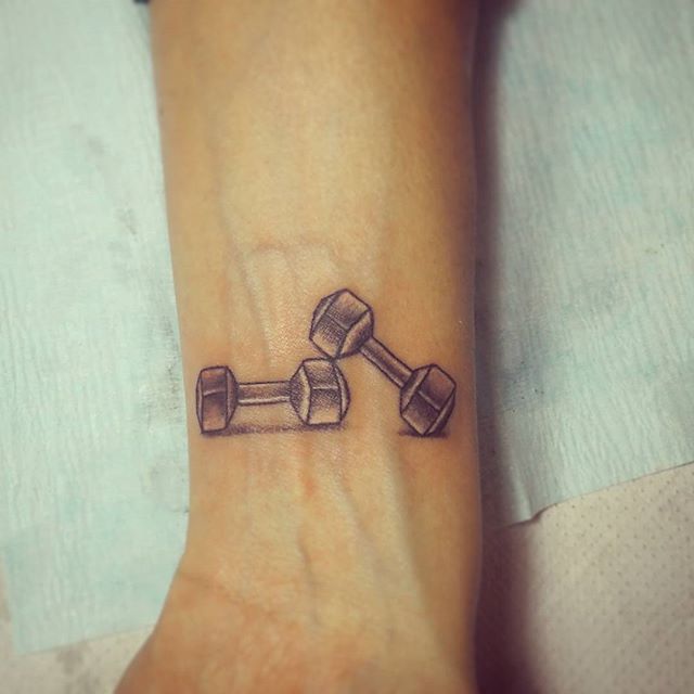 Chica con un tatuaje en el brazo de unas mancuernas