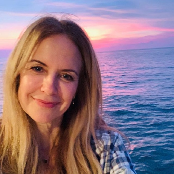 Kelly Preston y detrás de ella el mar y un hermoso atardecer