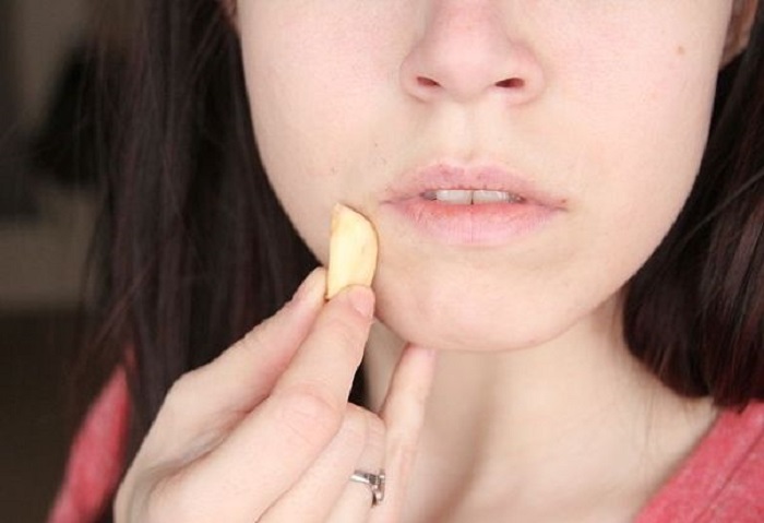 Chica aplicando un trozo de ajo en su rostro