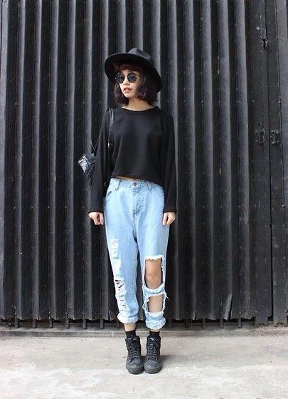 Chica con pantalones rotos, suéter negro y sombrero negro