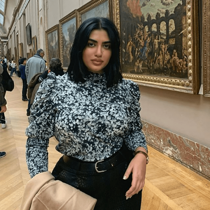 chica de cabello castaño corto de talla extra, curvy con una blusa de manga larga estampada y pantalones negros a la cintura