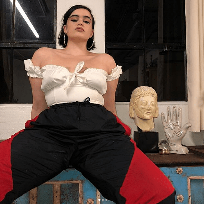 barbie ferreira usando un top blanco de manga corta con escote en v, pantalones negros con vistas rojas
