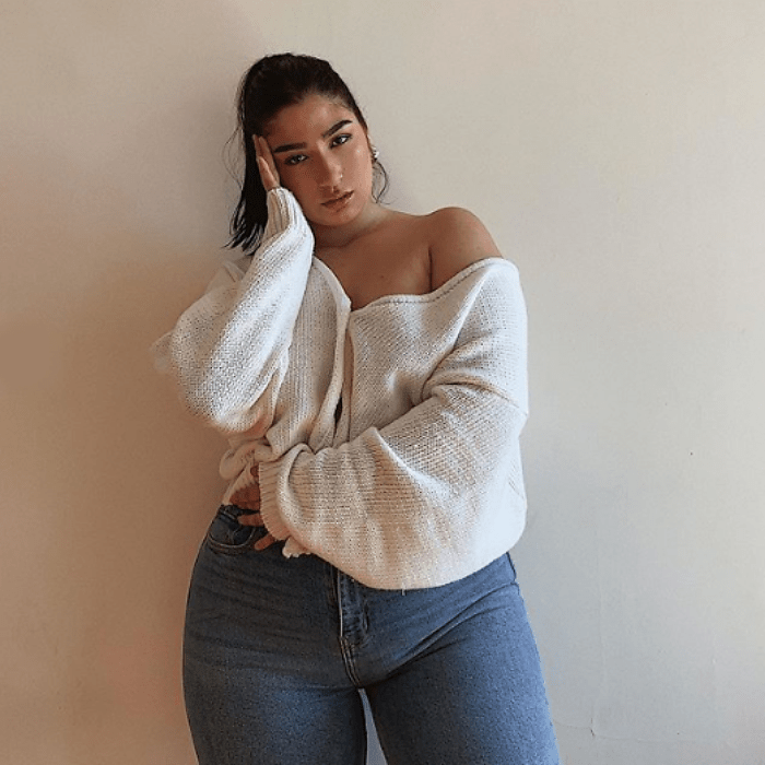 chica de cabello castaño largo usando una blusa tejida blanca sin hombros de manga larga con jeans a la cintura