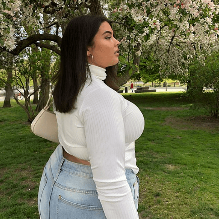 chica de cabello castaño largo usando una camiseta de manga larga y cuello alto con bolso de mano beige y jeans