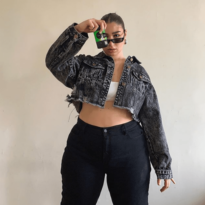 chica curvy talla extra usando un top blanco, una chaqueta cropped gris y jeans negros