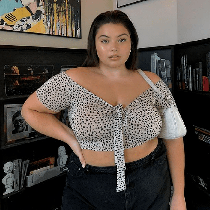 chica con cabello castaño largo curvy de talla extra usando una blusa crop top con escote en v y manga corta, jeans negros high waist y bolsa de mano blanca