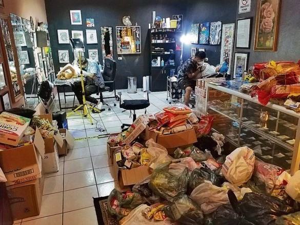 Hombres realizando tatuajes en un estudio repleto de víveres para donación