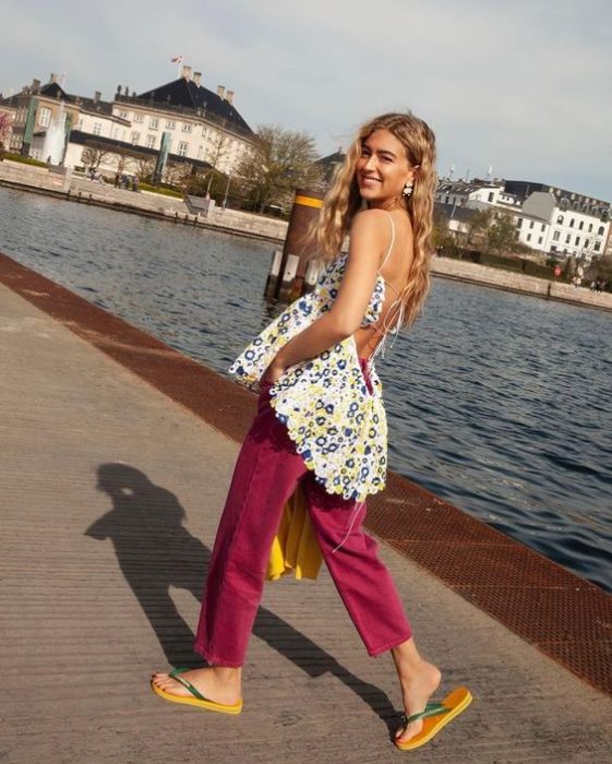 Chica rubia caminando por un lago con pantalón rosa y flip flops