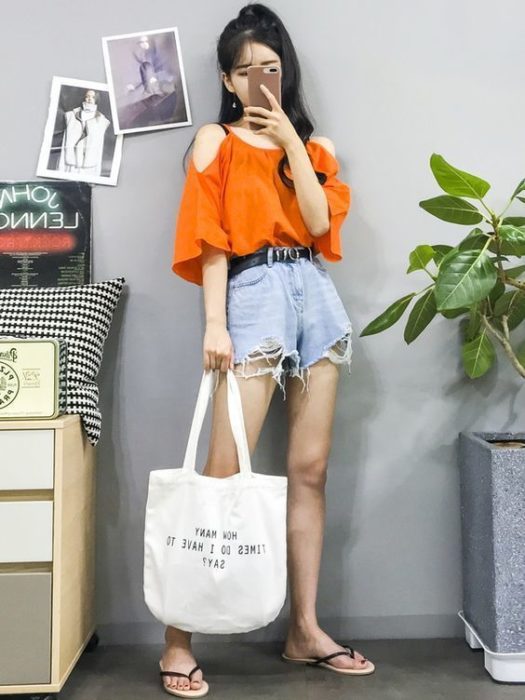 Chica asiática con blusa holgada naranja, shorts de mezclilla y flip flops