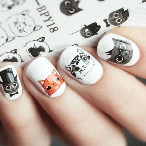 Manicura en tono blanco con stickers de gatos en tonos naranja