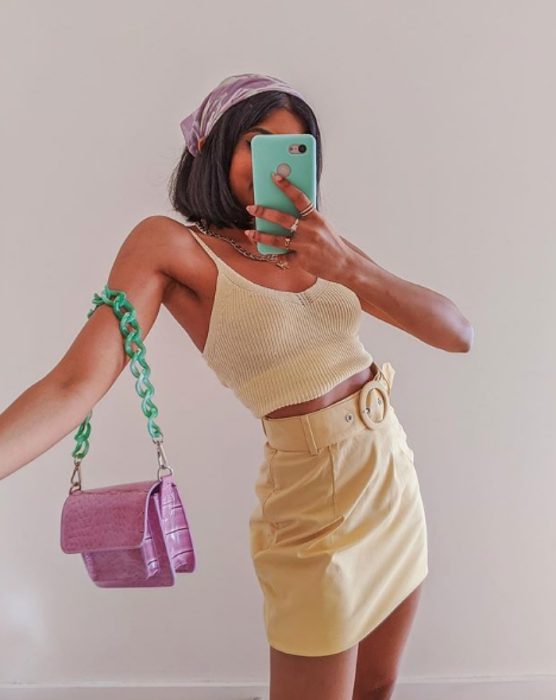 chica de piel morena usando un top y falda de color amarillo claro, un bolso lila con verde menta y un pañuelo en el cabello