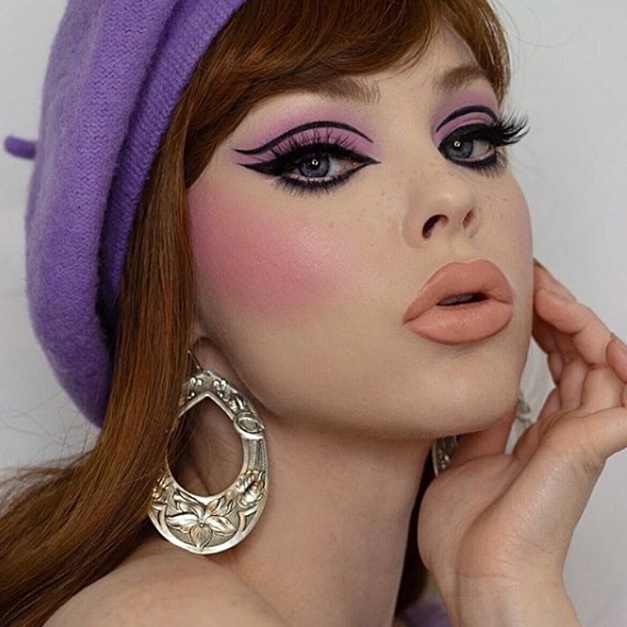 chica de cabello castaño claro con boina morada, usando sombra de ojos rosa, delineado cat-eye negro, lipstick matte nude y aretes grandes de plata