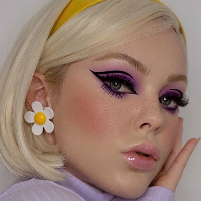 chica rubia con aretes de margarita, sombra de ojos color lila, delineado negro tipo cat-eye y diadema amarilla