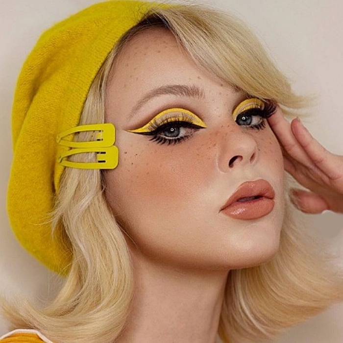 chica rubia con boina amarilla, usando maquillaje color amarillo, delineado tipo cat-eye y lipstick nude con gloss
