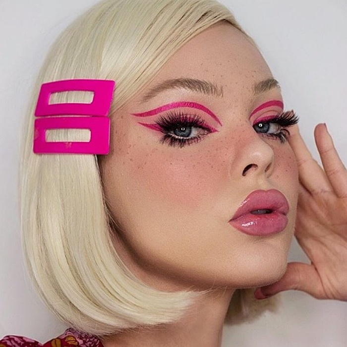 chica rubia usando broches grandes color fucsia, delineado rosa, pestañas postizas y labial rosa con gloss