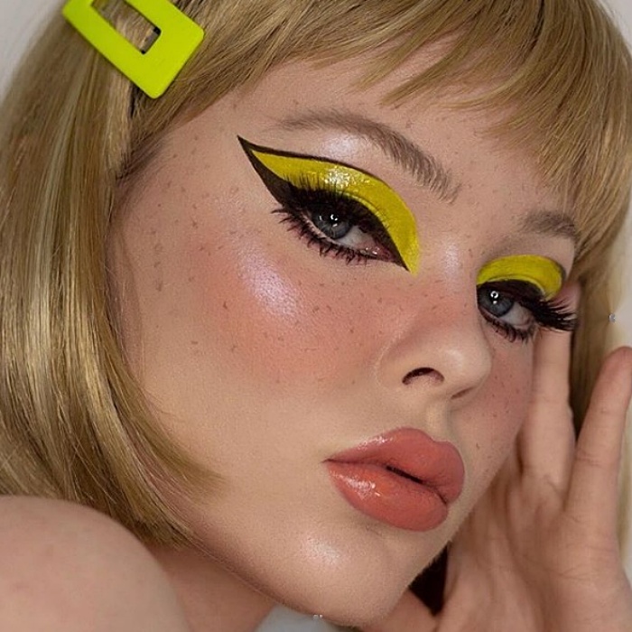 chica rubia usando sombra amarilla, delineado negro cat-eye y labial rosa