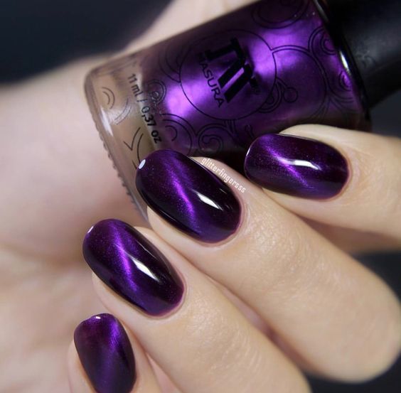 manos de mujer con manicura en tonos morado y negro con efecto ojo de gato