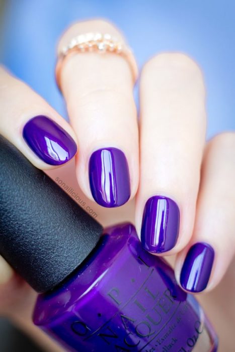 manos de mujer con manicura en tono morado uva brillante