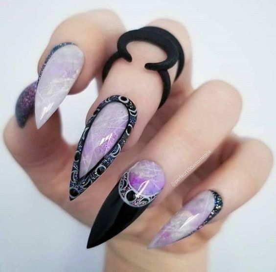 manos de mujer con manicura en tonos morado con efecto cuarzo y decoraciones en negro