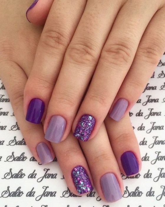 manos de mujer con manicura en tonos violeta, morado y púrpura con destellos de glitter
