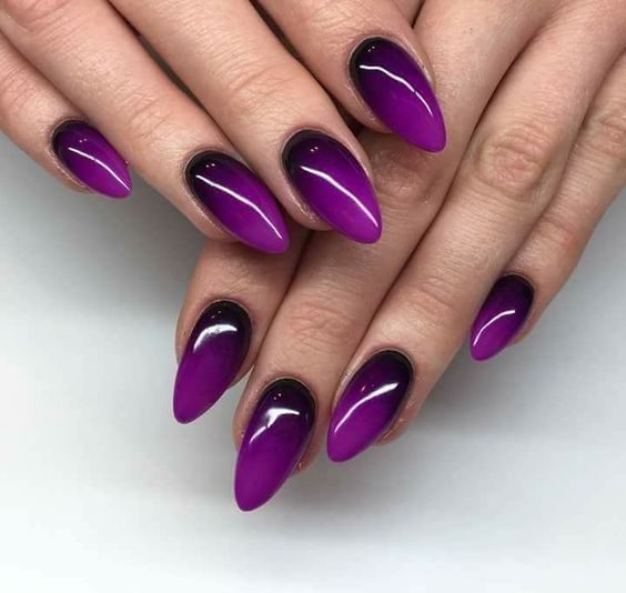 manos de mujer con manicura en tonos púrpura con efecto degradado en estilo almendra