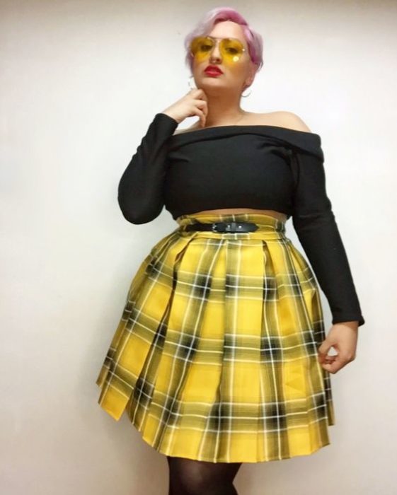 Modelo plus size posa con blusa sin hombros negra y falda de cuadros amarilla