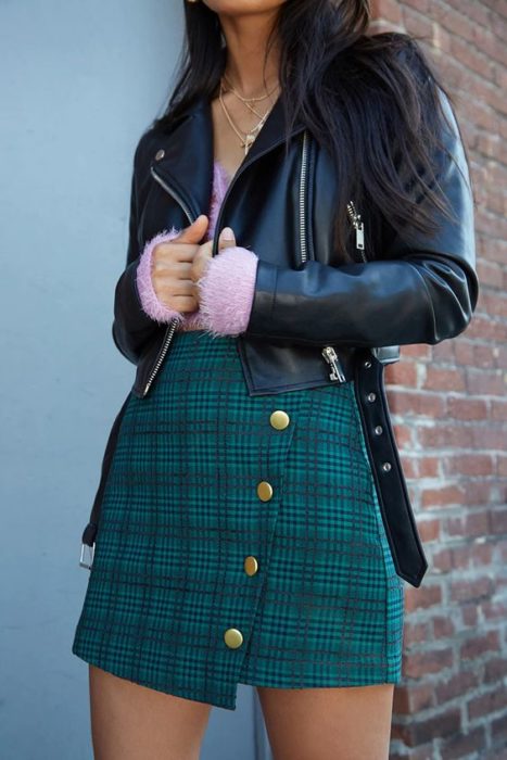Chica usando chaqueta de cuero, suéter rosa y falda verde de cuadros