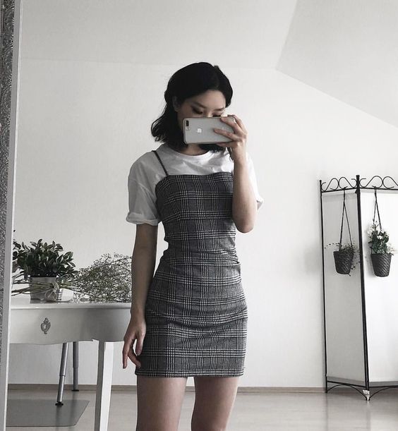 Chica se toma una foto frente al espejo con blusa blanca y vestido pegado de cuadros gris