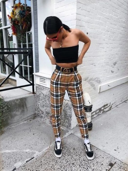 Chica ajustándose el pantalón y usando crop top negro con pantalón amarillo a cuadros