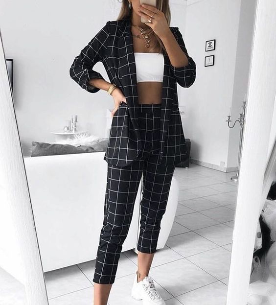 Mujer tomándose un selfie frente al espejo con blusa blanca y saco y pantalón de cuadros negros