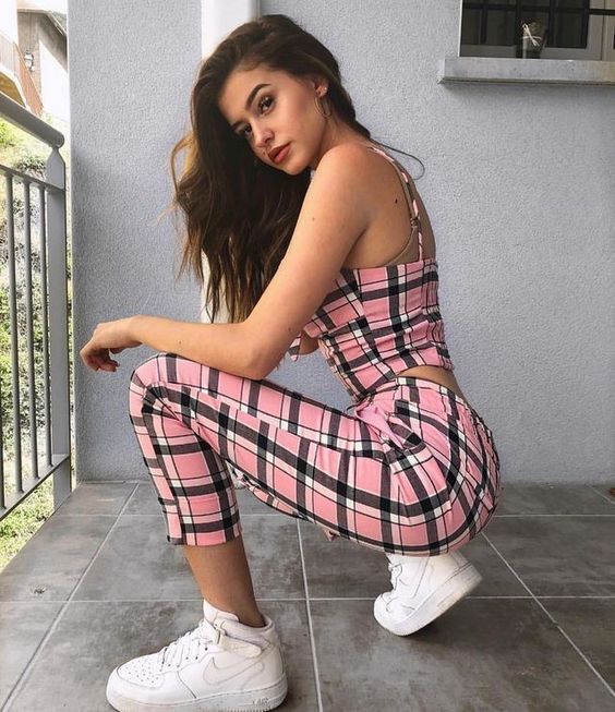 Chica agachada posando con traje completo de cuadros color rosa