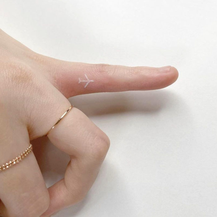 Tatuajes pequeños; minitatuaje de avión con tinta blanca en el dedo meñique