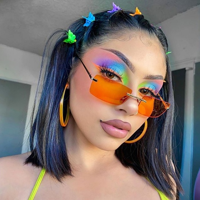 chica de cabello morado y azul usando maquillaje de arcoíris y gafas de sol anaranjadas