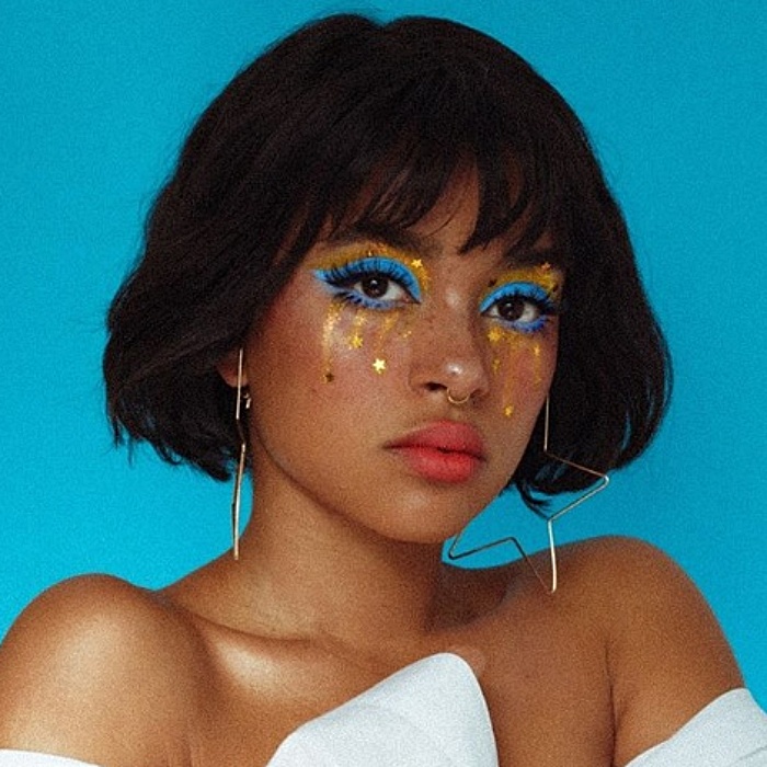chica morena con cabello corto usando maquillaje de sombras azules, glitter dorado y stickers de estrellas