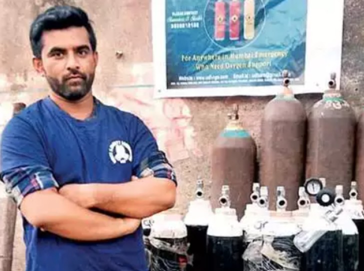 Hombre con brazos cruzados posando frente a diversos tanques de oxígeno que serán donados