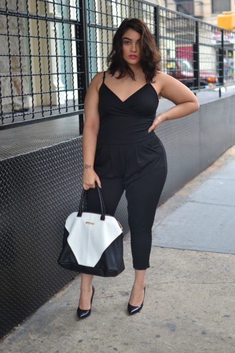 Chica curvy usando un jumpsuit de color negro con zapatillas negras y un bolso de color blanco