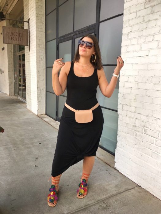 Chica curvy usando un vestido de color negro con una cangurera de color café y sandalias de colores