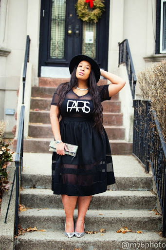 Chica curvy con un vestido de color negro con un sombrero y clutch de color gris
