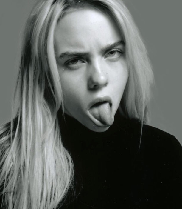 Fotografía en blanco y negro de Billie Eilish sacando la lengua, con cabello suelto